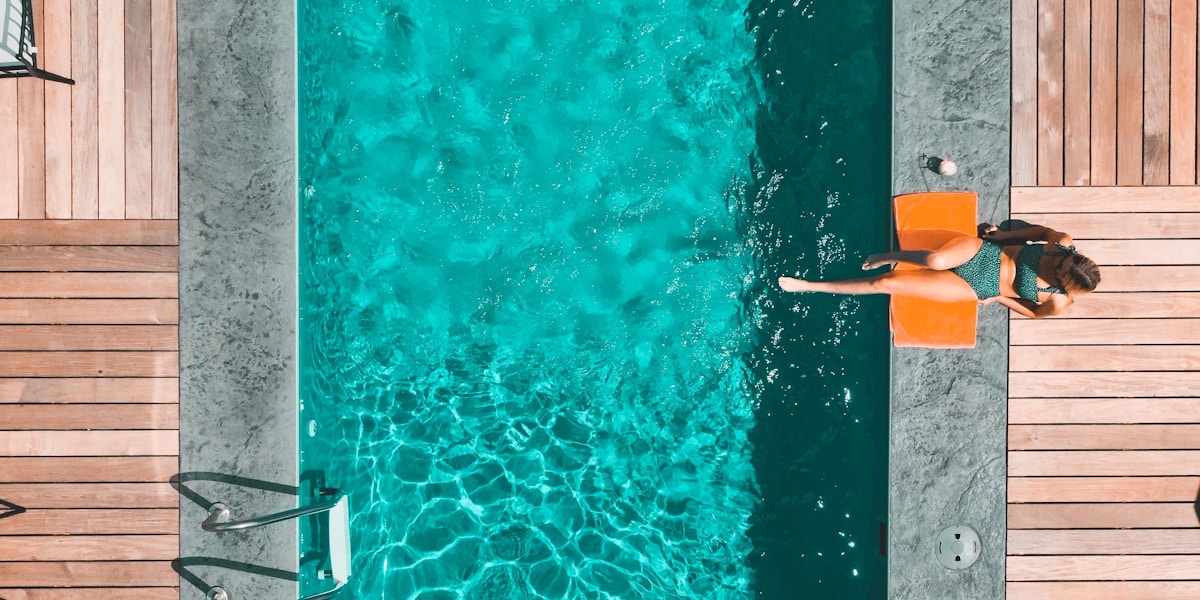 Homeowner performing pool maintenance with a skimmer net beside a backyard pool